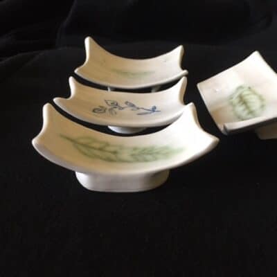 la photo représente quatre supports à baguette ou soucoupe de présentation bouchée sushi. ces support sont en porcelaine et sur l'intérieur en terre incrustée apparaissent les motifs feuilles