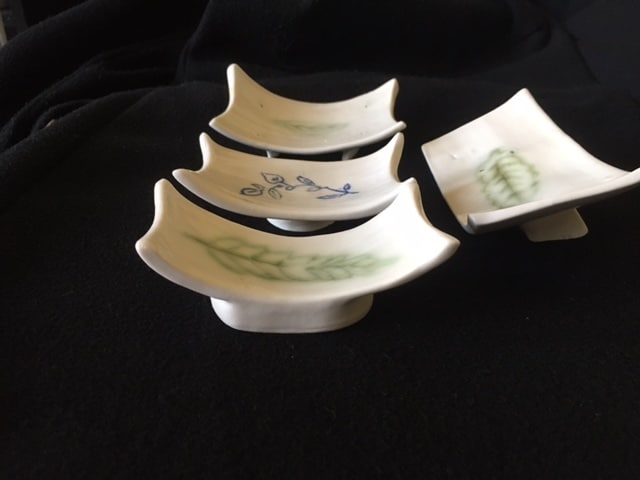 la photo représente quatre supports à baguette ou soucoupe de présentation bouchée sushi. ces support sont en porcelaine et sur l'intérieur en terre incrustée apparaissent les motifs feuilles